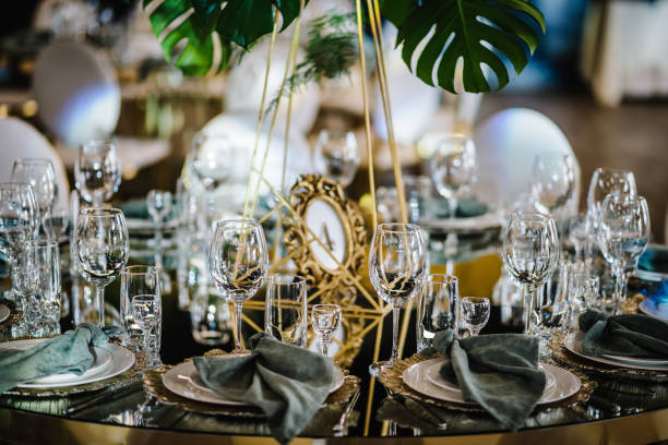 istock Round served banquet tables ready for guests, decorated table with plate, glasses, forks, emerald green napkins. Elegant dinner table. Beautifully organized event. Wedding hall with atmospheric decor. 1489421024