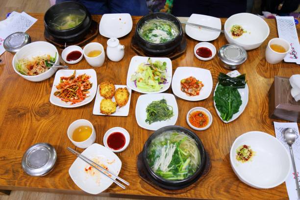 Korean traditional meal of buckwheat noodles, kimchi, lettuce for wraps, pickled radish, and banchan side dishes on a wooden table