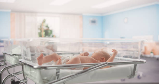 adorable caucasian newborn child lying in hospital bed in a nursery clinic. little playful and healthy baby. medical health care, maternity and parenthood concept - hospital nursery imagens e fotografias de stock