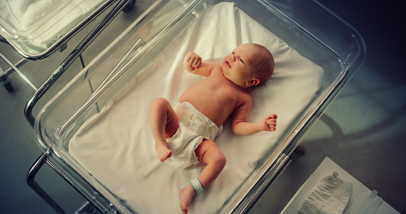 Adorable Small Caucasian Newborn Child Lying in Hospital Bed in a Nursery Clinic. Little Playful and Healthy Baby. Medical Health Care, Maternity and Parenthood Concept. High Angle Close Up Portrait