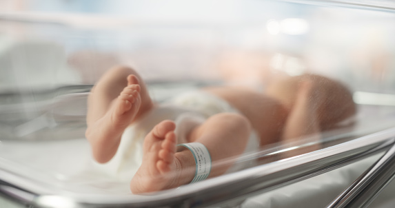 Lindo bebé recién nacido caucásico acostado en moisés en un hospital de maternidad. Retrato de un pequeño niño juguetón y enérgico con una etiqueta de identificación con nombre en la pierna. Concepto de atención médica, embarazo y maternidad photo