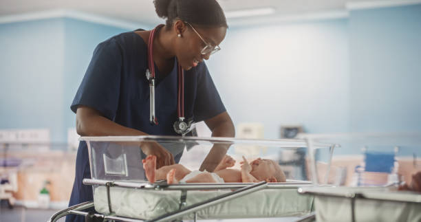 保育園で愛らしい小さな白人の新生児をなだめるプロのアフリカ人看護師。医療ヘルスケア、産科病院、親子関係のコンセ��プト - maternity clinic ストックフォトと画像