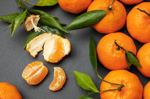 Orange tangerines with green leaves on a gray background. Tangerine without peel, peeled parts. Top view.