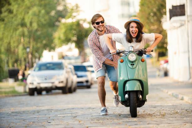Laughing couple riding on a scooter in town Laughing couple riding on a scooter in town. Guy pushing a moped. Adventure and vacations concept moped stock pictures, royalty-free photos & images