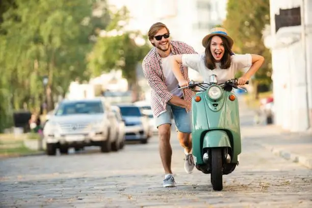 Laughing couple riding on a scooter in town. Guy pushing a moped. Adventure and vacations concept