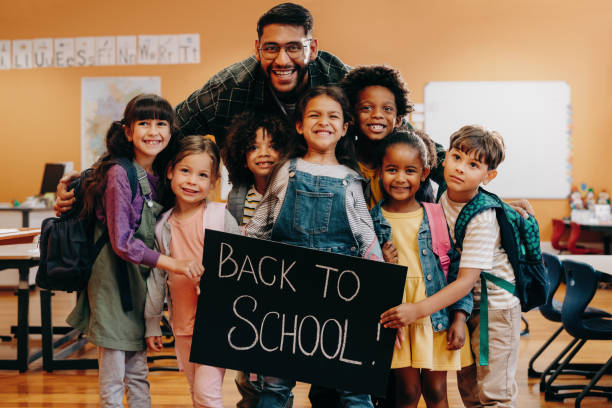 Teacher and his primary school class holding a back to school sign, excited to start a new year stock photo