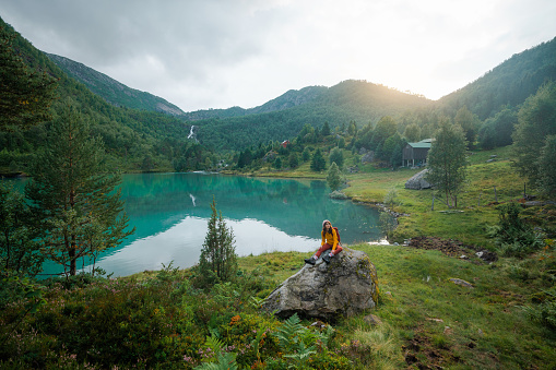 Woman in colourful outfit  sitting  on the  rock on the background of mountain lake and looking at view