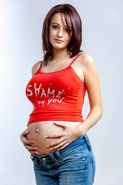 depressed looking pregnant young woman with brown hair in jeans and sleeveless top holding her big belly