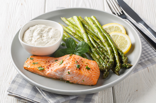 Delicious baked salmon with crispy asparagus served with tartar sauce close-up in a plate on the table. Horizontal