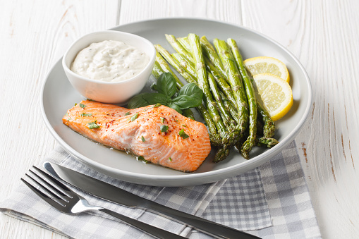 Wild salmon fillet with asparagus served with tartar sauce and lemon close-up in a plate on the table. Horizontal
