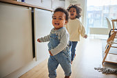 Baby boy and his older brother running through their kitchen at home