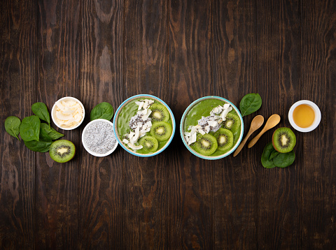 Green smoothie bowl with organic Spinach, Banana, Chia Seeds, fresh kiwi on dark wooden background. Vegan, Food and drink, healthy dieting and nutrition, alkaline, vegetarian concept.