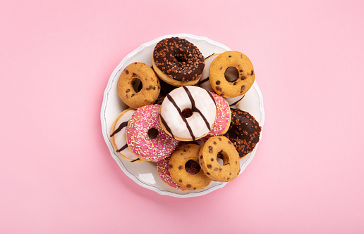 Holiday colorful Donuts doughnuts with chocolate and sugar sprinkles on pink background, top view. Festive carnival or birthday party card. Happy National donut day Concept.