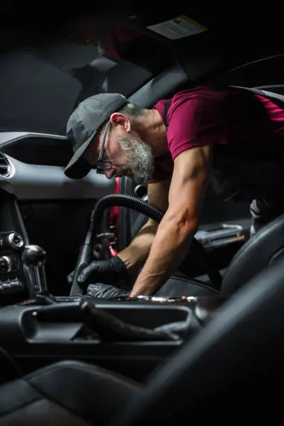 Specialist Professional Car Cleaning and Detailing Company Vacuum Cleaning an Ecological Perforated Black Faux Leather Interior in a Modern Sportscar. Worker Cleaning Every Little Seam on the Car Seat