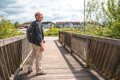 Mature Asian male walking outdoors. Standing on a wooden bridge in a public park.