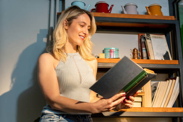 istock Woman standing in front of bookshelf reading a book 1489459548