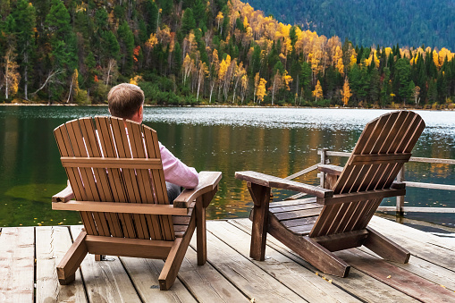 A senior man  enjoying a lake view from  Adirondack chairs , autumn.