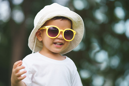 Portrait of Happy Asian Chinese little child boy wearing hat and yellow sunglasses smiling outdoor