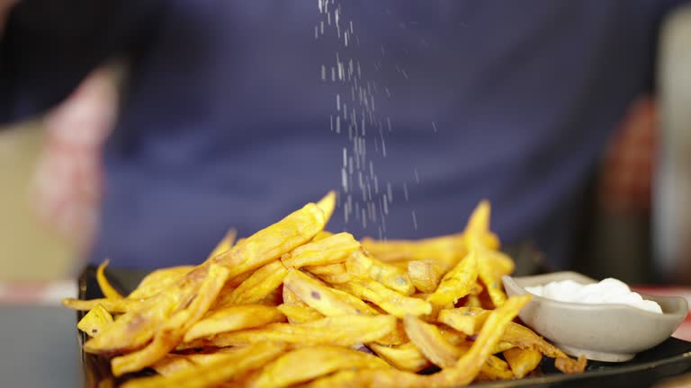 Slow motion shot of salt being sprinkled over a french fries.