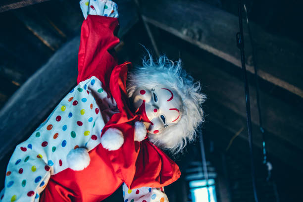 An evil toy clown doll hanging from the rafters of an old and spooky attic.