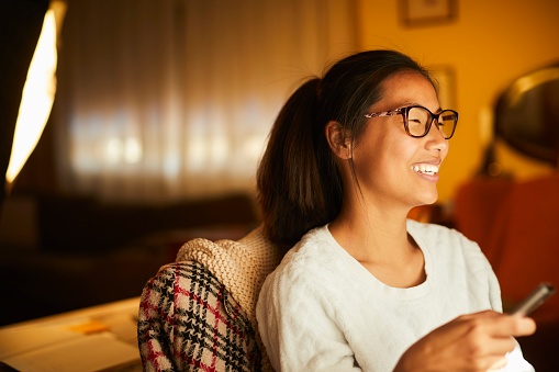 A close-up view of a woman holding a remote control, her gaze focused on an out-of-frame television. A smile graces her face as she engages with the content displayed on the screen