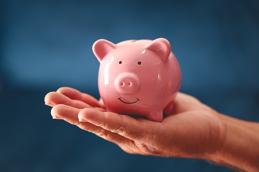 A piggy bank in a man's hand in close-up photo. Blue background.