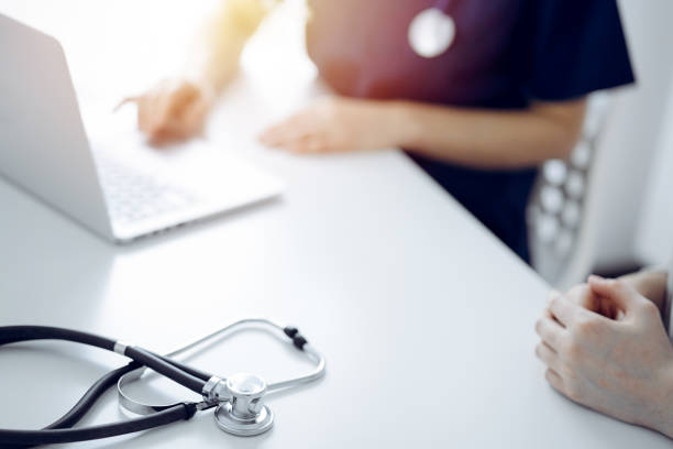 istock Stethoscope lying on the tablet computer in front of a doctor and patient using laptop computer at the background. Medicine, healthcare concept 1489475601