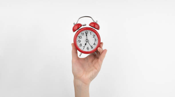 istock A woman's hand holds a red alarm clock against a white wall 1489480527