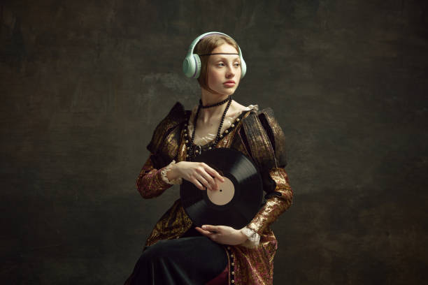 портрет красивой молодой девушки, королевской особы в элегантном винтажном платье, слушающей музыку в наушниках, держащей винил на темно-з� - medieval music стоковые фото и изображения
