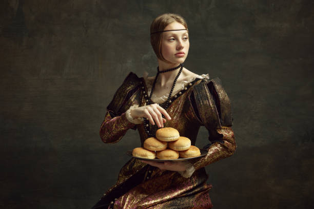 portret młodej, eleganckiej, pięknej dziewczyny w stroju vintage, sukienki trzymającej bułeczki burgerowe na ciemnozielonym tle - century zdjęcia i obrazy z banku zdjęć