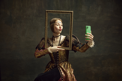Retrato de una niña bonita, persona real con vestido vintage sosteniendo el marco de fotos y tomándose una selfie con el teléfono sobre un fondo verde oscuro. photo