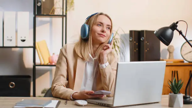 Photo of Young businesswoman working on laptop at home office wearing headphones listening favorite music