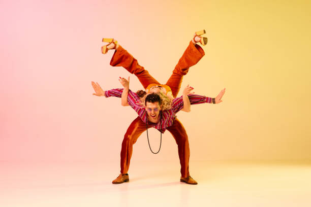 Dynamic image of artistic, beautiful couple, man and woman in stylish clothes dancing against gradient pink yellow background Dynamic image of artistic, beautiful couple, man and woman in stylish clothes dancing against gradient pink yellow background. Concept of retro style, dance, fashion, art, hobby, music, 70s man dancing disco in vintage 1970s outfit stock pictures, royalty-free photos & images
