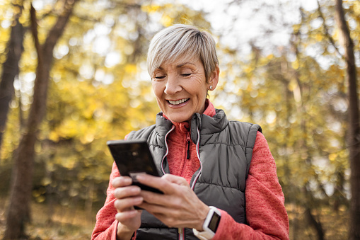 Senior woman with short gray hair using phone while standing in public park