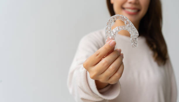 close up woman hand holding dental aligner retainer (invisible) on background for beautiful teeth and dental treatment course concept close up woman hand holding dental aligner retainer (invisible) on background for beautiful teeth and dental treatment course concept dental equipment hand stock pictures, royalty-free photos & images