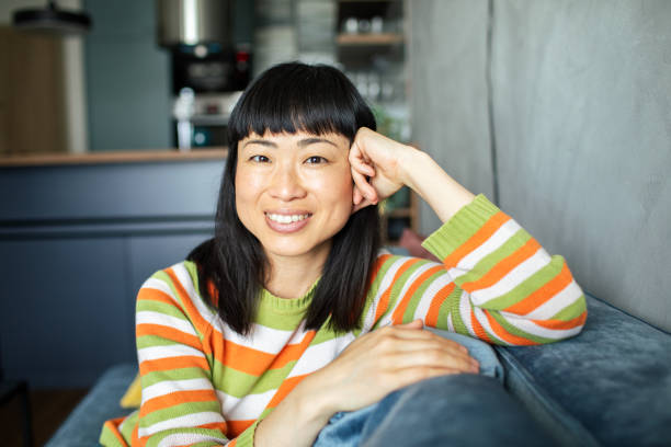 istock Young Japanese woman smiling while sitting on a couch and looking at the camera 1489496630