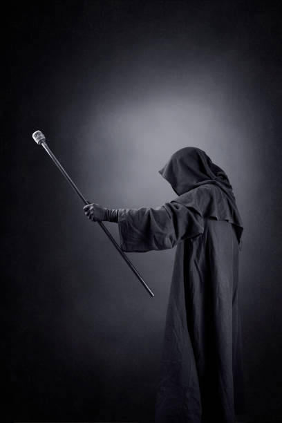 Wizard with hooded cape and magic staff over dark misty background
