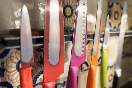 Colorful Knife Set Hanging in Kitchen - Well worn and used knives hanging on magnetic rack in home kitchen.