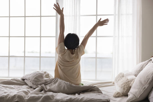 istock Satisfied relaxed middle aged lady sitting on bed, rising hands 1489504378