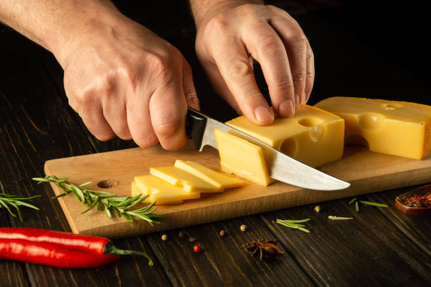 istock Hands of a cook with a knife cut cheese on a cutting board before preparing pizza. Dark space for recipe 1489506428