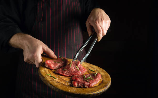 istock The cook holds a cutting board with raw beef steaks before barbecue. Preparation for roasting meat with rosemary and spices. Black space for restaurant recipe or hotel menu 1489507851