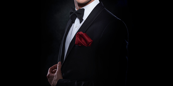 Elegant young man in suit on dark background.