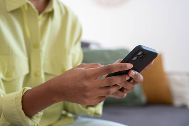 Hands of young dark skinned woman with finger rings using online app on mobile phone, making call, browsing Internet, chatting on social media, holding cellphone, texting, typing message. Close up manos de una joven de piel oscura con anillos en los dedos usando la aplicación en línea en el teléfono móvil, haciendo llamadas, navegando por internet, chateando en las redes sociales, sosteniendo el teléfono celular, enviando mensajes de texto, esc