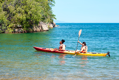 Two tourists in canoe, Mumbo Island, Lake Malawi, Malawi, Africa. Mumbo Island, within Lake Malawi National Park, is in the Salima District 100 kilometers east of the capital Lilongwe. Malawi, the landlocked country in southeastern Africa, is a country of highlands split by the Great Rift Valley and the huge Lake Malawi, whose southern end is within Lake Malawi National Park and several other parks are now habitat for diverse wildlife from colorful fish to the Big Five. Cape Maclear is known for its beach resorts, whilst several islands offer rest and recreation.