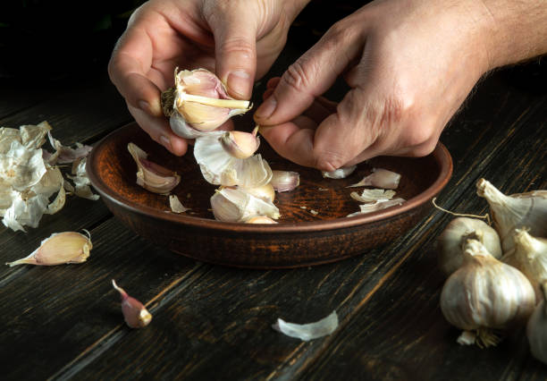 istock The cook cleans the garlic in a vintage plate on the kitchen table before preparing a vegetarian meal. Tasty recipe concept on dark background 1489511498