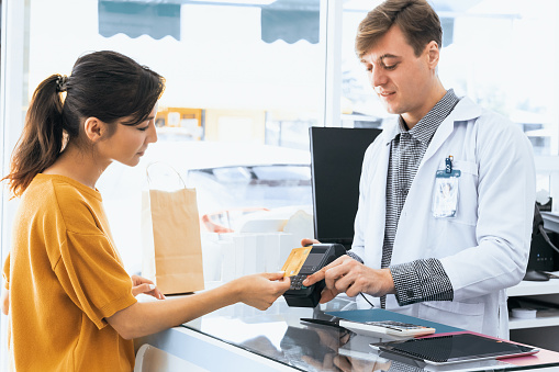 Payment by credit card with payment terminal in qualified drugstore. Modern financial payment of electric money. Satisfied customer purchase medication in pharmacy with prescription from pharmacist.