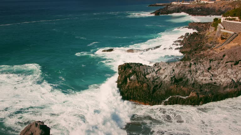 Powerful stormy ocean waves break on stone shore and natural swimming pool on Tenerife. Charco de Isla Cangrejo. Historical landmark. Piscina natural.