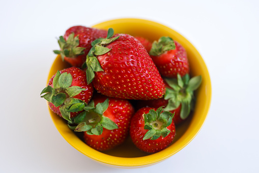A bowl of fresh red strawberries in a yellow bowl on a white background