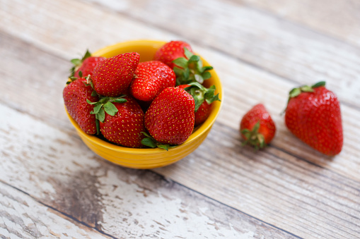 A bowl of fresh red strawberries in a yellow bowl on a table