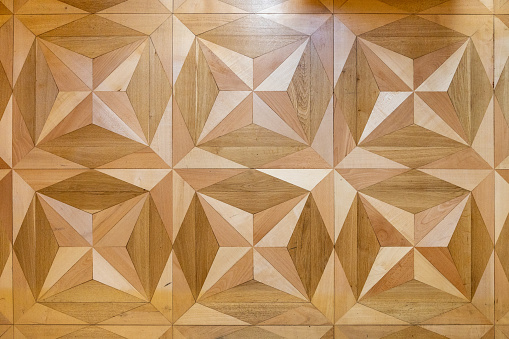 Star-shaped historic wood flooring with lacquered surface partially reflecting window light